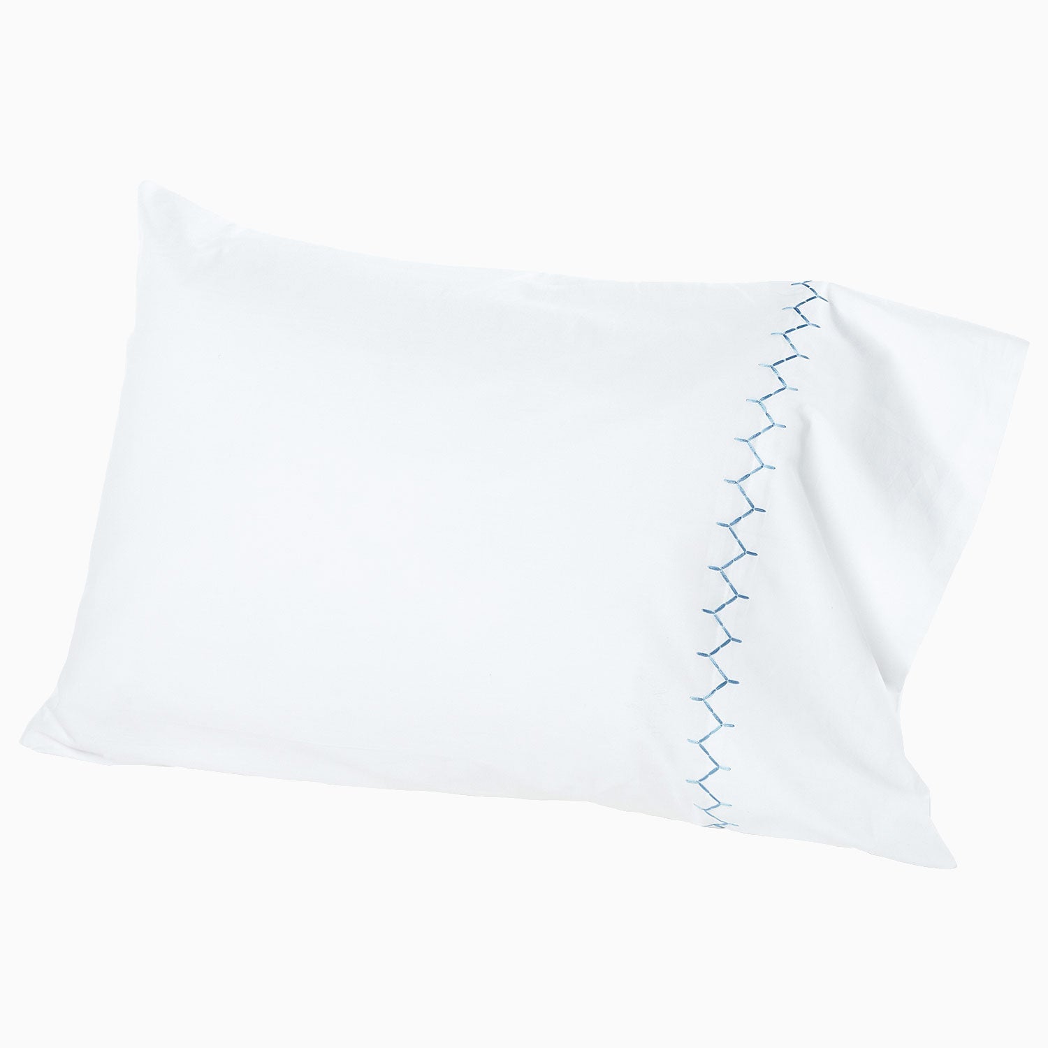 A white pillow with blue embroidered designs will be replaced with the Stitched Light Indigo Organic Sheets by John Robshaw.